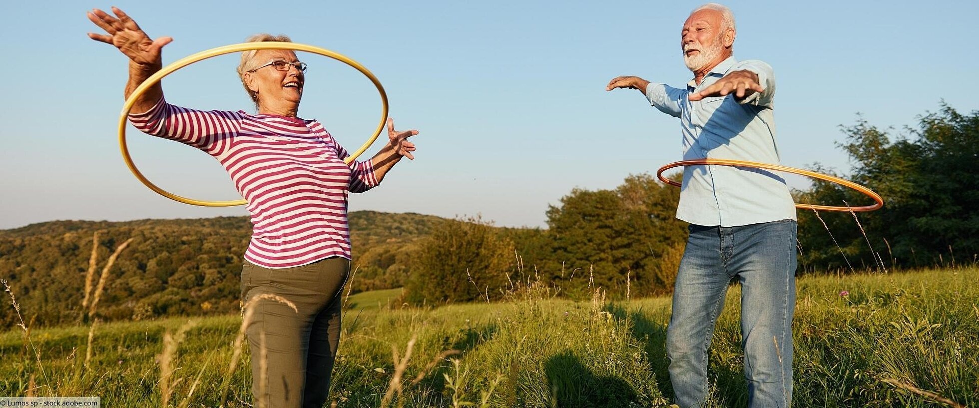 Ältere Frau und älterer Mann mit Hulahoop-Reifen auf einer Wiese