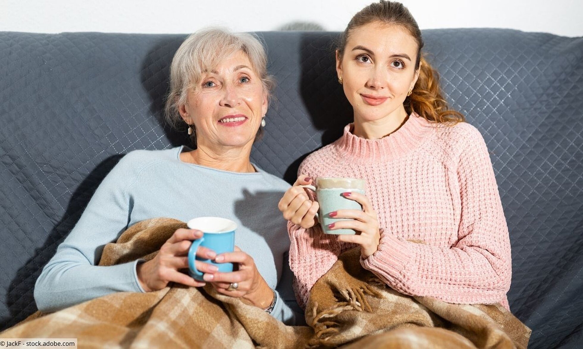 Mutter und erwachsene Tochter sitzen mit Tee auf dem Sofa.
