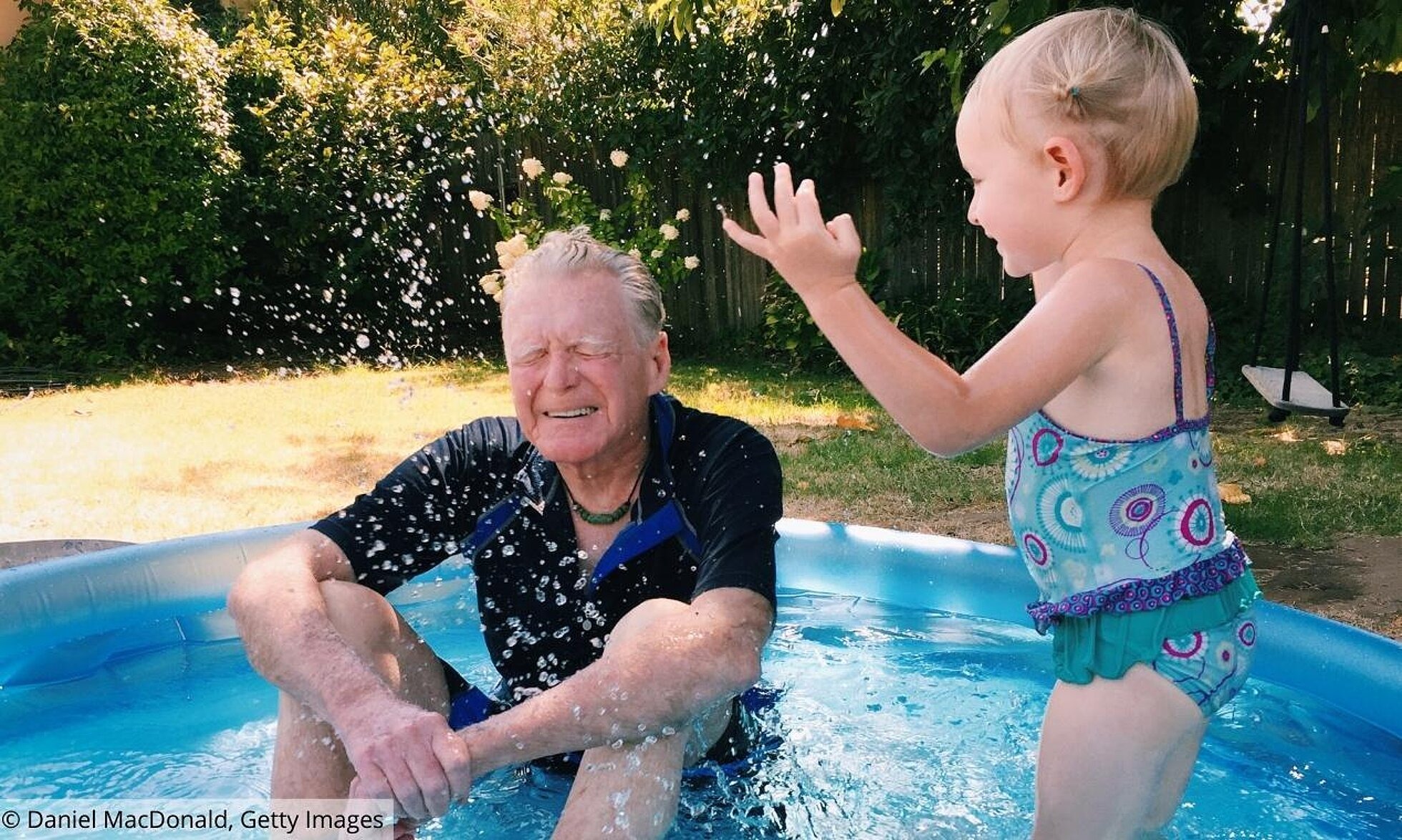 Älterer Mann mit Kind im Pool wird nass gespritzt
