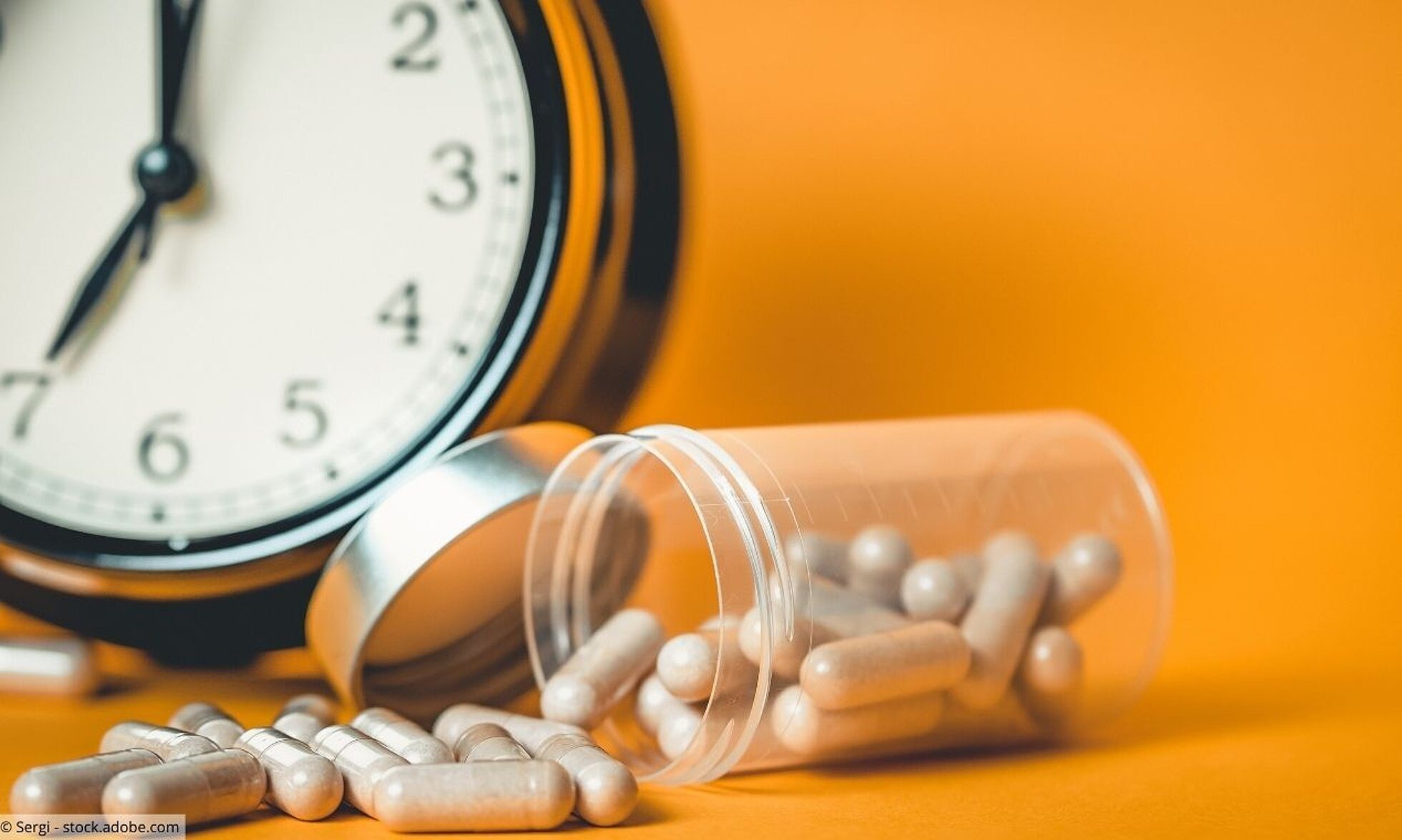 Dose mit Tabletten, große Uhr im Hintergrund