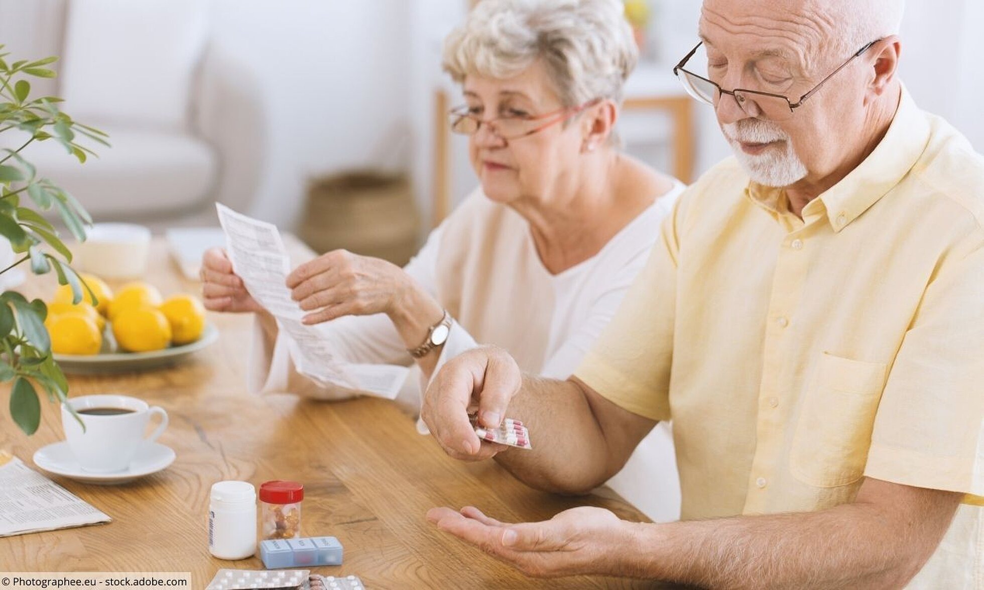 Älteres Paar am Frühstückstisch. Er nimmt Tabletten. Sie liest Beipackzettel.