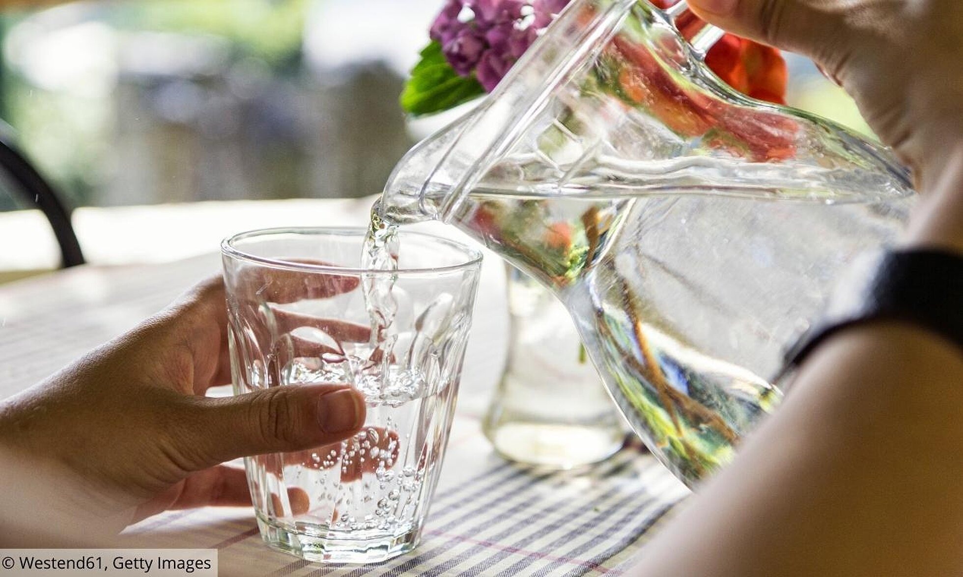 Person gießt Wasser aus einer Glaskaraffe in ein Glas