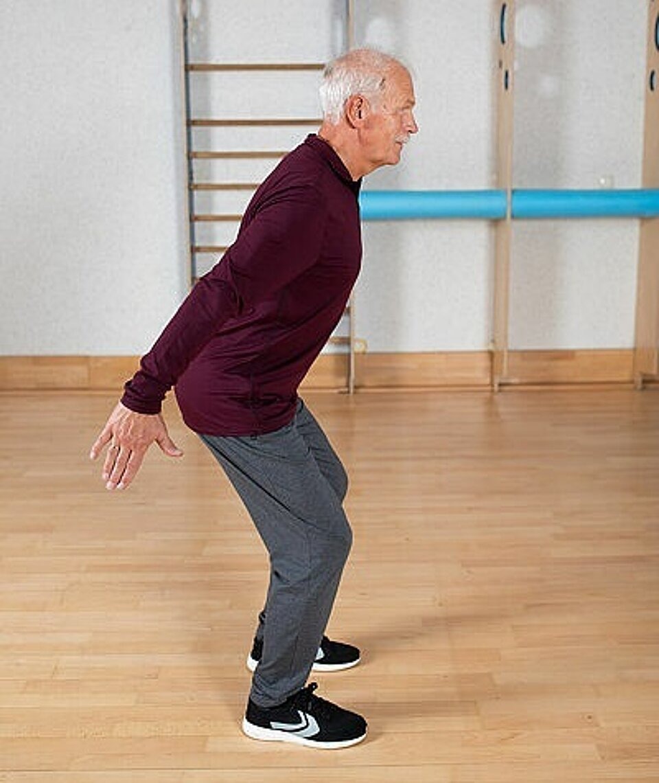 Älterer Mann macht in einem Gymnastikraum Kniebeugen
