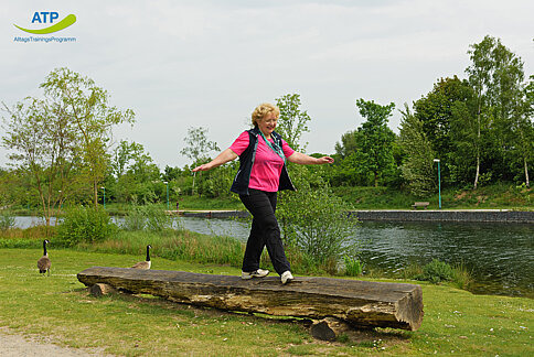 Ältere Frau balanciert auf einem Baumstamm