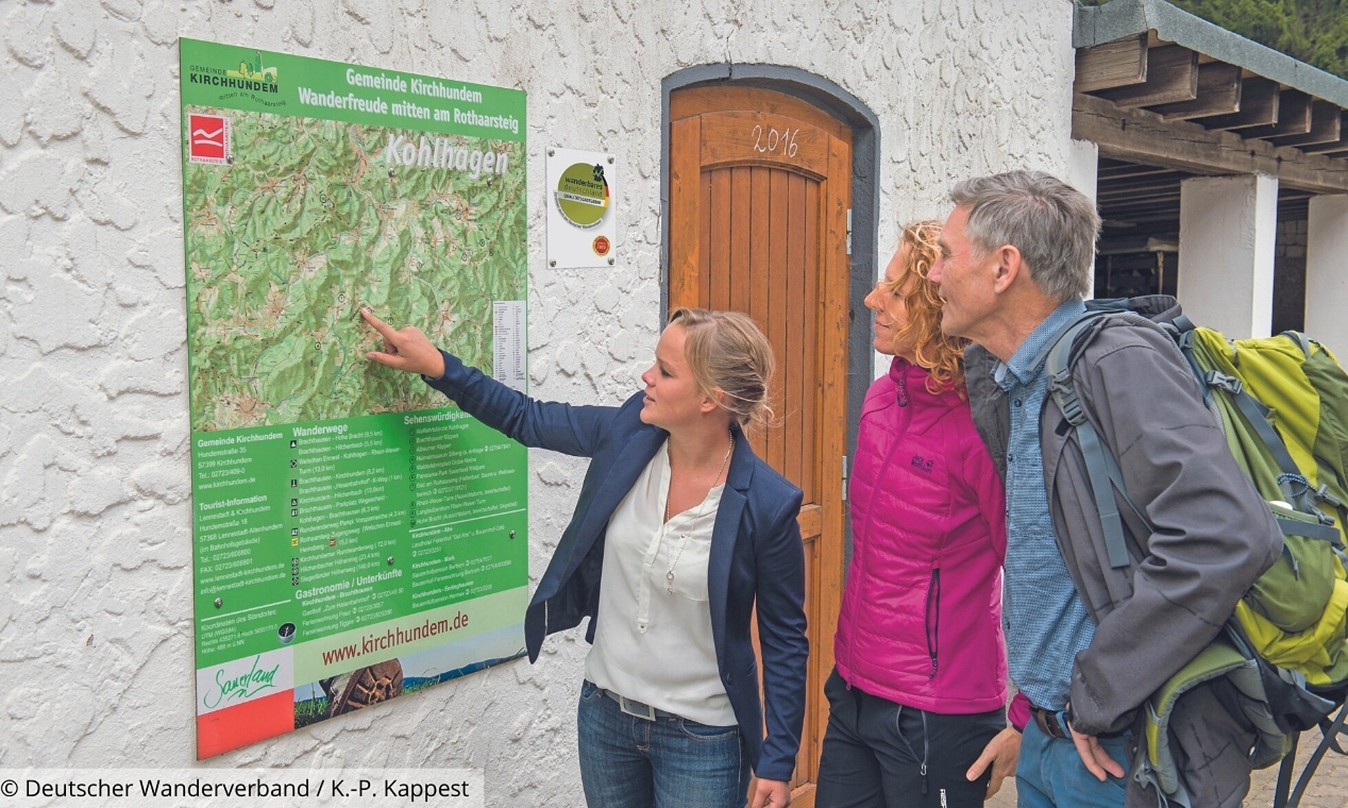 Frau mit zwei Wanderern zeigt auf Wanderplan
