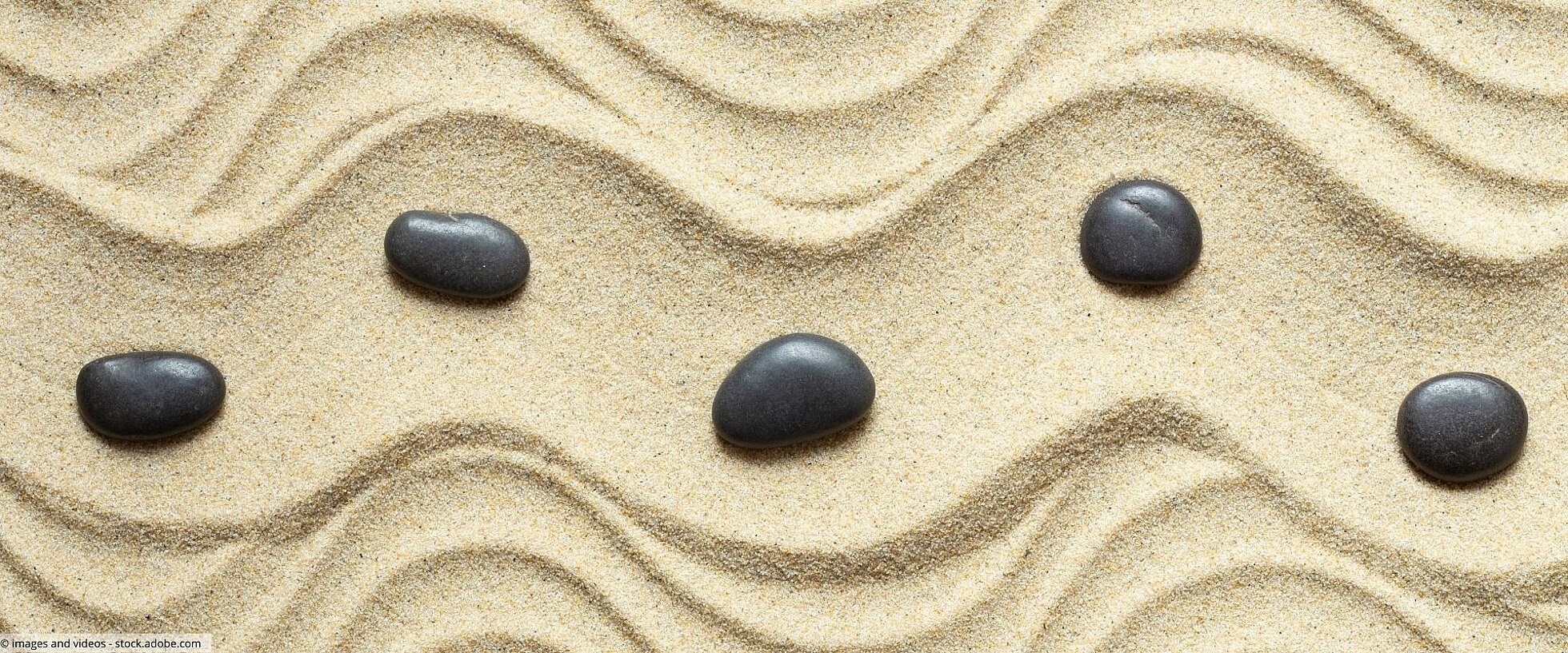 Wellenlinien im Sand mit schwarzen Steinen