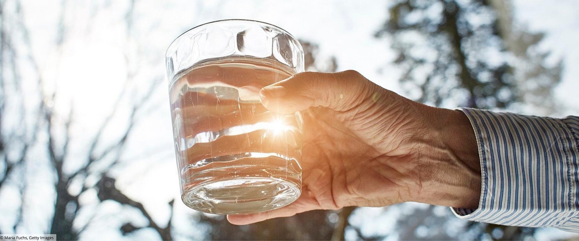 Hand eines Seniors hält ein Glas Wasser