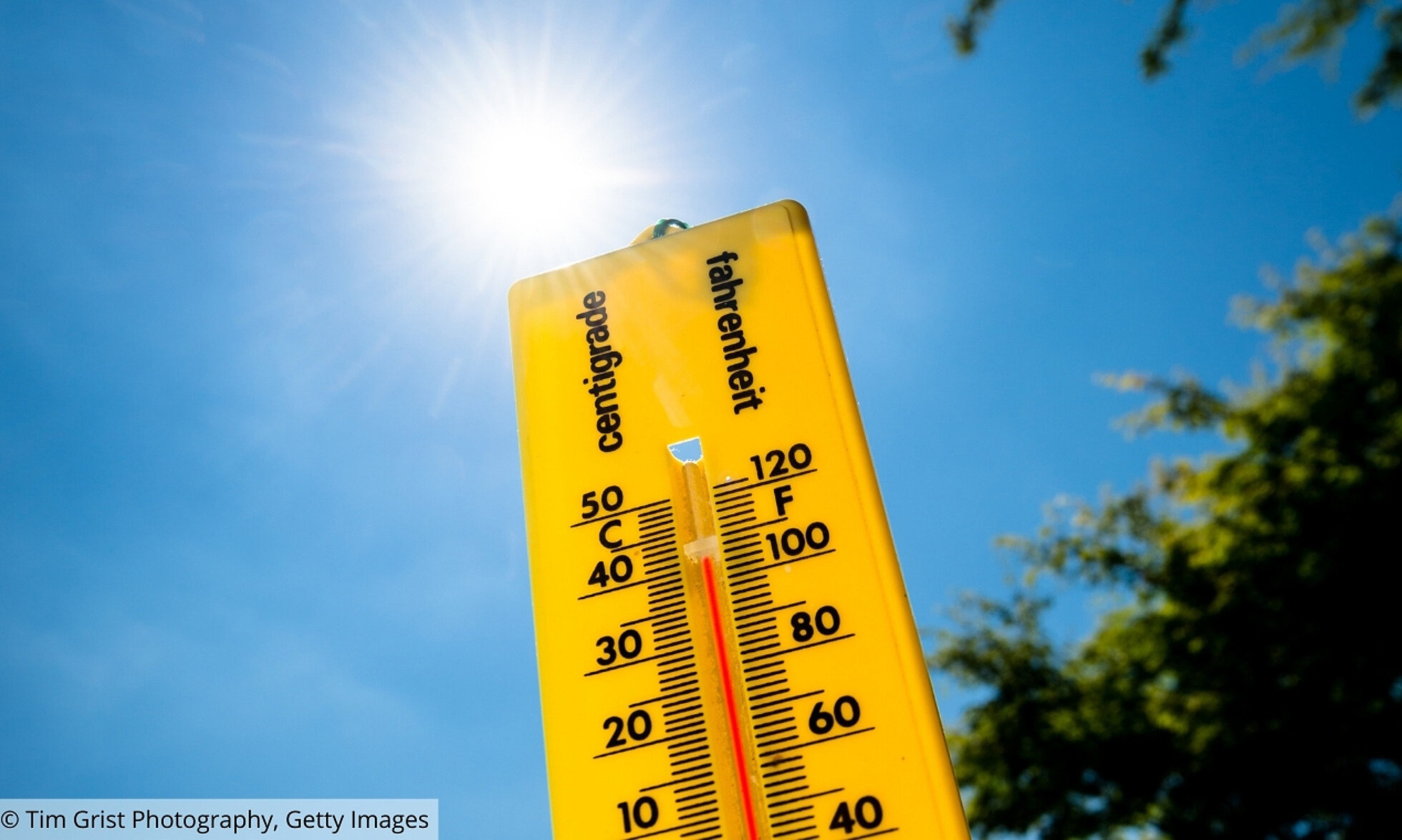 Gelbes Thermometer vor blauen Himmel und Sonnenschein