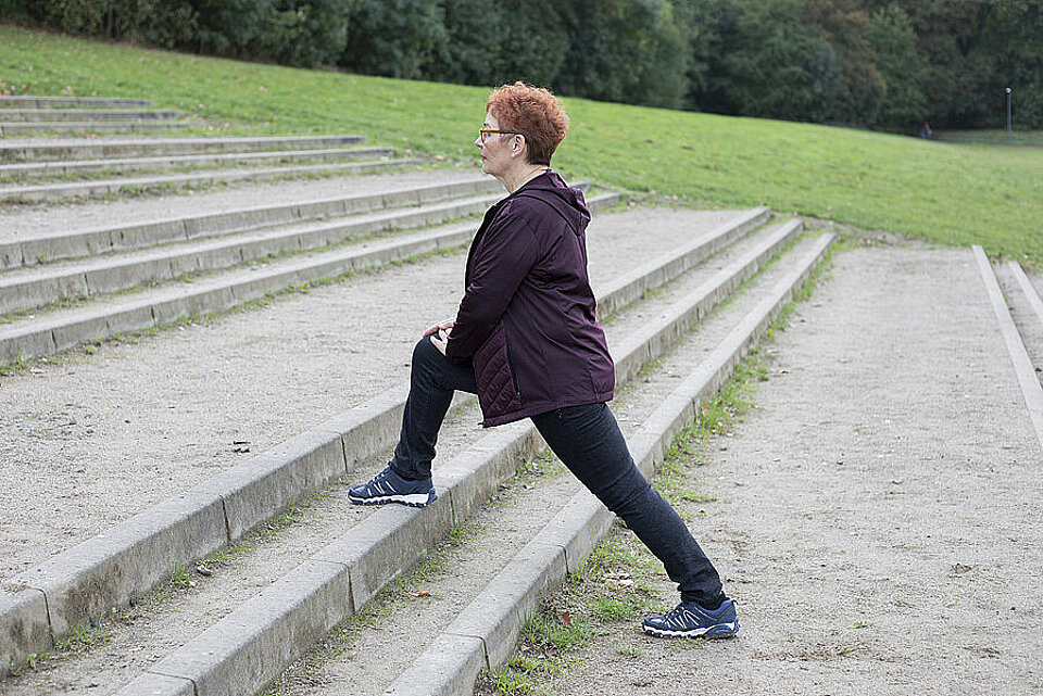 Frau dehnt rechtes Bein auf Treppenstufe.