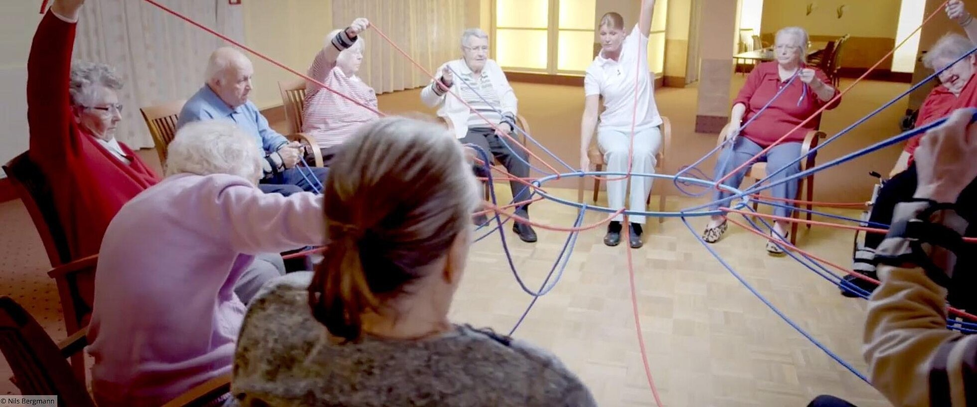 Gruppe von älteren Menschen hält mit Seilen einen Ring fest.