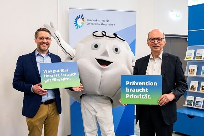 Bundeskonferenz Gesundes Alter 2026: Dr. NIeßen und Dr. Aluttis mit Maskottchen