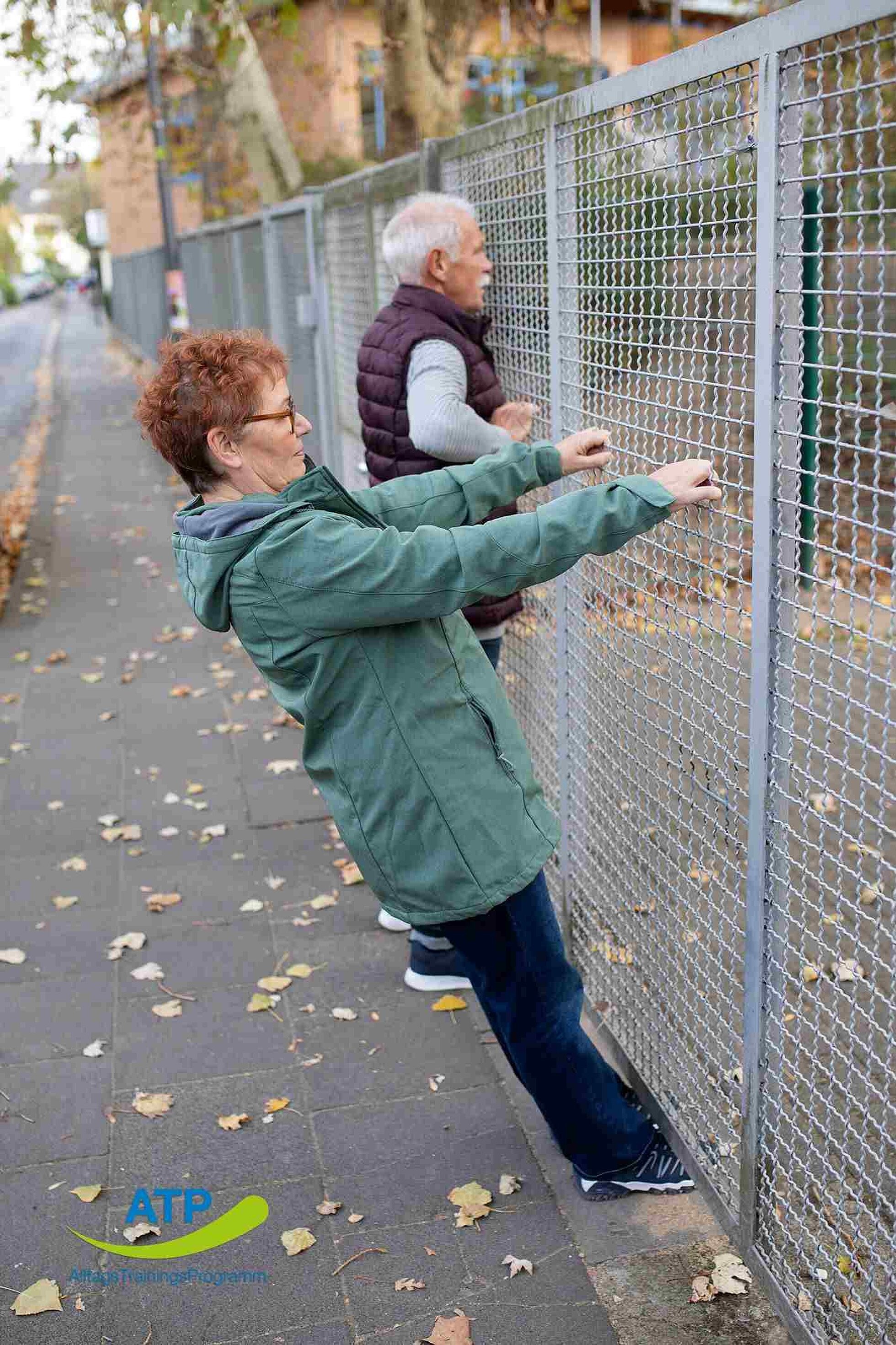 ATP-Dauerangebot Übung 9 Ältere Frau bei Ruderbewegung an einem Zaun