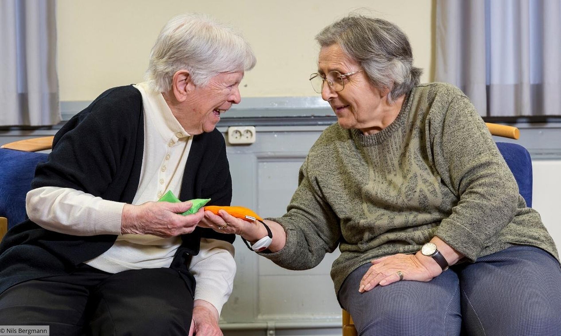 2 sitzende Seniorinnen bei Bewegungsübungen mit Bohnensäckchen