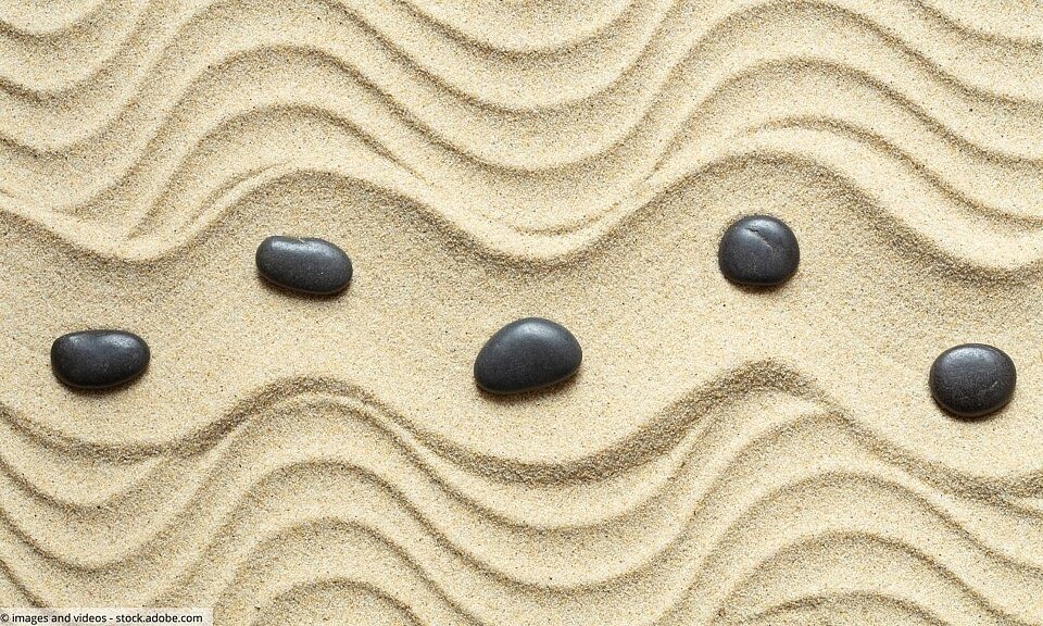 Wellenlinien im Sand mit schwarzen Steinen