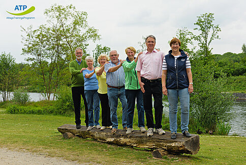 7 ältere Menschen balancieren auf einem Baumstamm