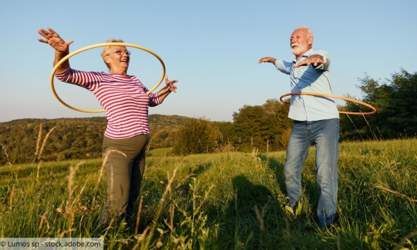 Ältere Frau und älterer Mann mit Hulahoop-Reifen auf einer Wiese