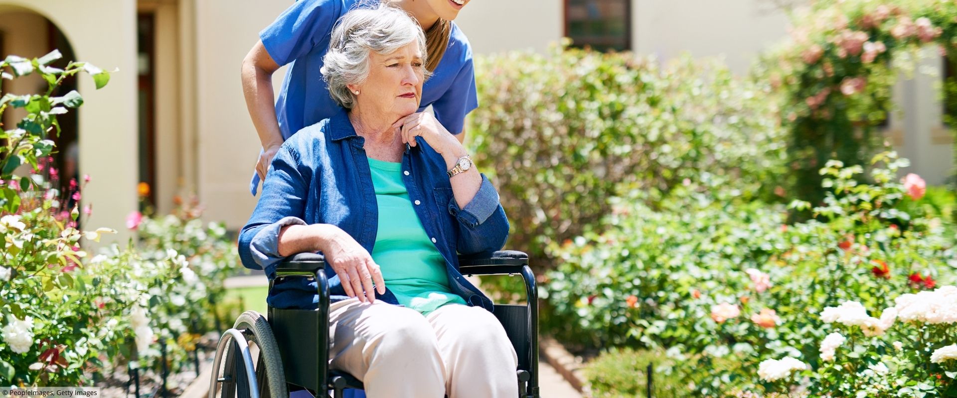 Pflegekraft schiebt Seniorin im Rollstuhl